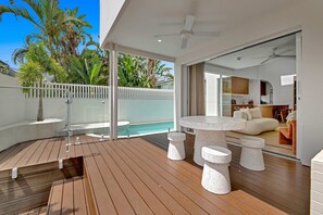 A modern outdoor deck with a pool, wooden flooring, and a seating area with a table and stools. - Villa Laya, Palm Beach (Palm Beach)