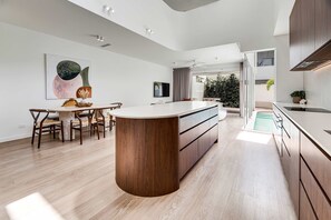 A modern kitchen with a central island, wooden cabinets, and a dining area with a table and chairs. - Villa Laya, Palm Beach (Palm Beach)