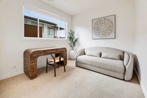 Una sala de estar moderna con un escritorio curvo de madera, un sofá color beige, un ventanal grande y una obra de arte abstracta colgada en la pared.