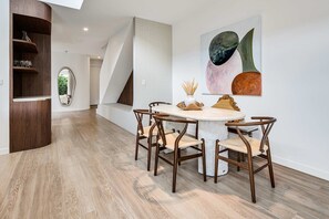 A modern dining area with a round table, wooden chairs, and a large abstract painting on the wall. - Villa Laya, Palm Beach (Palm Beach)