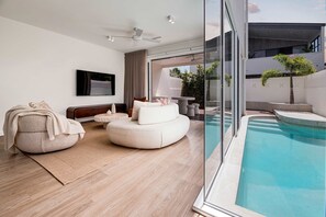 A modern living room with a pool, a sofa, a rug, and a ceiling fan. - Villa Laya, Palm Beach (Palm Beach)