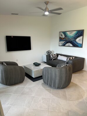 A modern living room with a flat-screen TV, a ceiling fan, a marble coffee table, and a gray sofa set. - Cozy 2-bedroom condo in gorgeous Wellen Park Golf and Country Club (Venice)