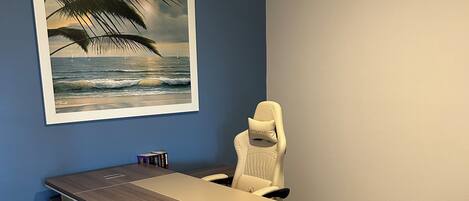 A home office with a desk, chair, and a framed picture of a beach scene.