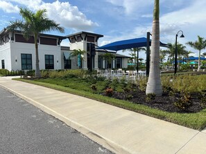 A modern building with a white facade, a blue awning, and a landscaped area with palm trees and chairs. - Cozy 2-bedroom condo in gorgeous Wellen Park Golf and Country Club (Venice)