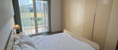Un dormitorio con cama, armario, ventana con cortinas y lámpara colgante.