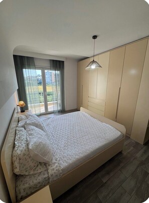 A bedroom with a bed, a wardrobe, a window with curtains, and a hanging light fixture. - Spacious Family Stay in Astir, Tirana • Sleeps 6+ (Kashar)
