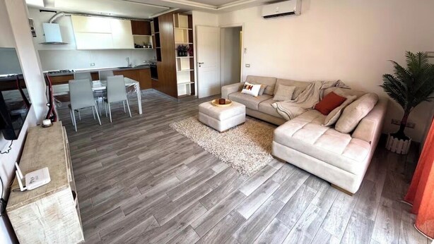 Een moderne woonkamer met een bank, voetenbankje en een eethoek met stoelen.