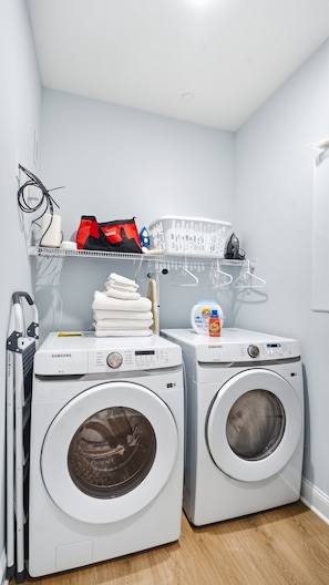 A laundry area with two front-loading washing machines, a drying rack, and a shelf with laundry supplies. - Modern 3BR condo with Pool & Private garage (Wildwood)