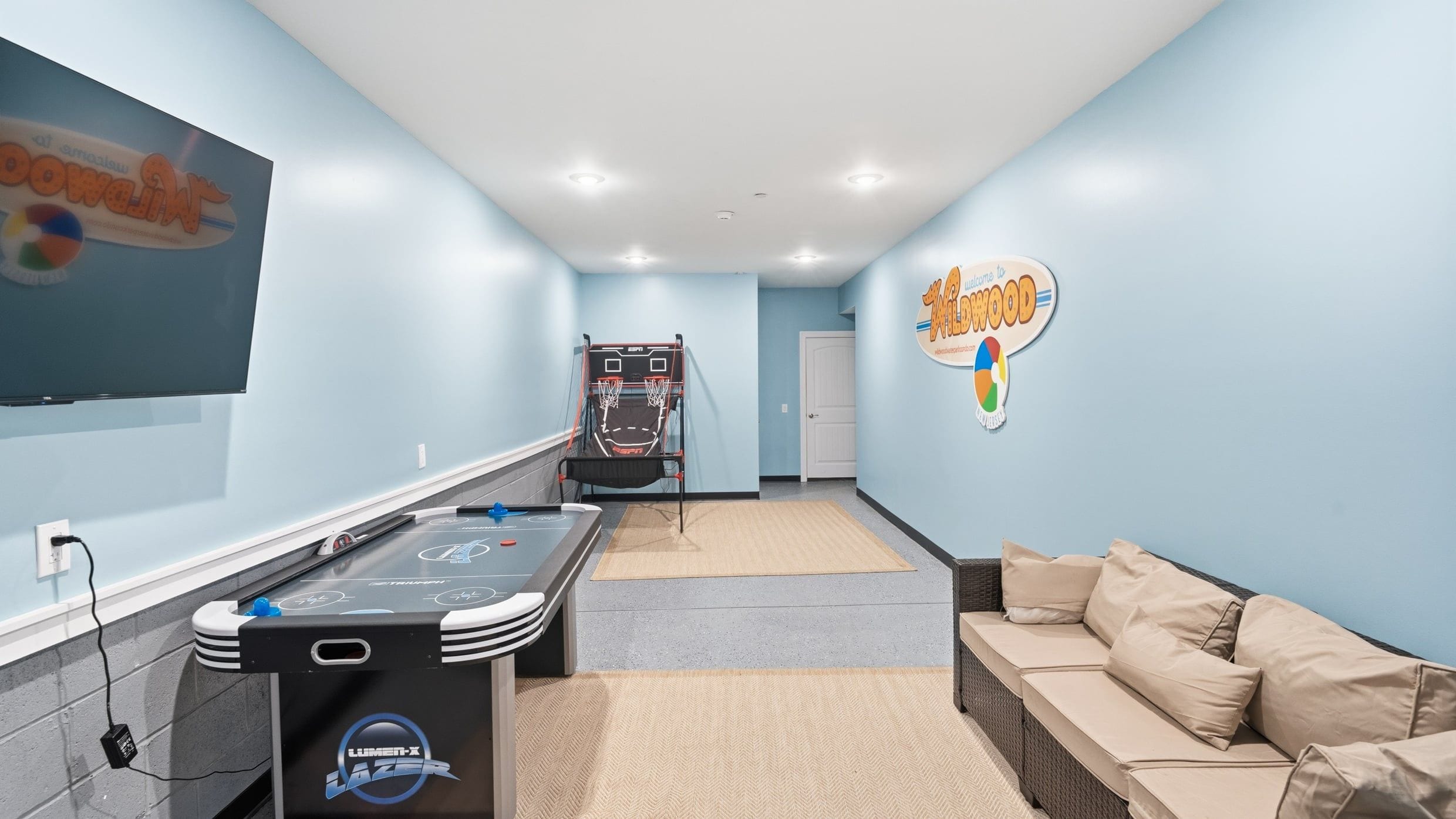 Una habitación con mesa de juego tipo shuffleboard, un sofá y un cartel en la pared.