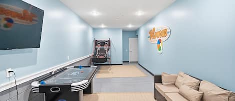 Una habitación con mesa de juego tipo shuffleboard, un sofá y un cartel en la pared.