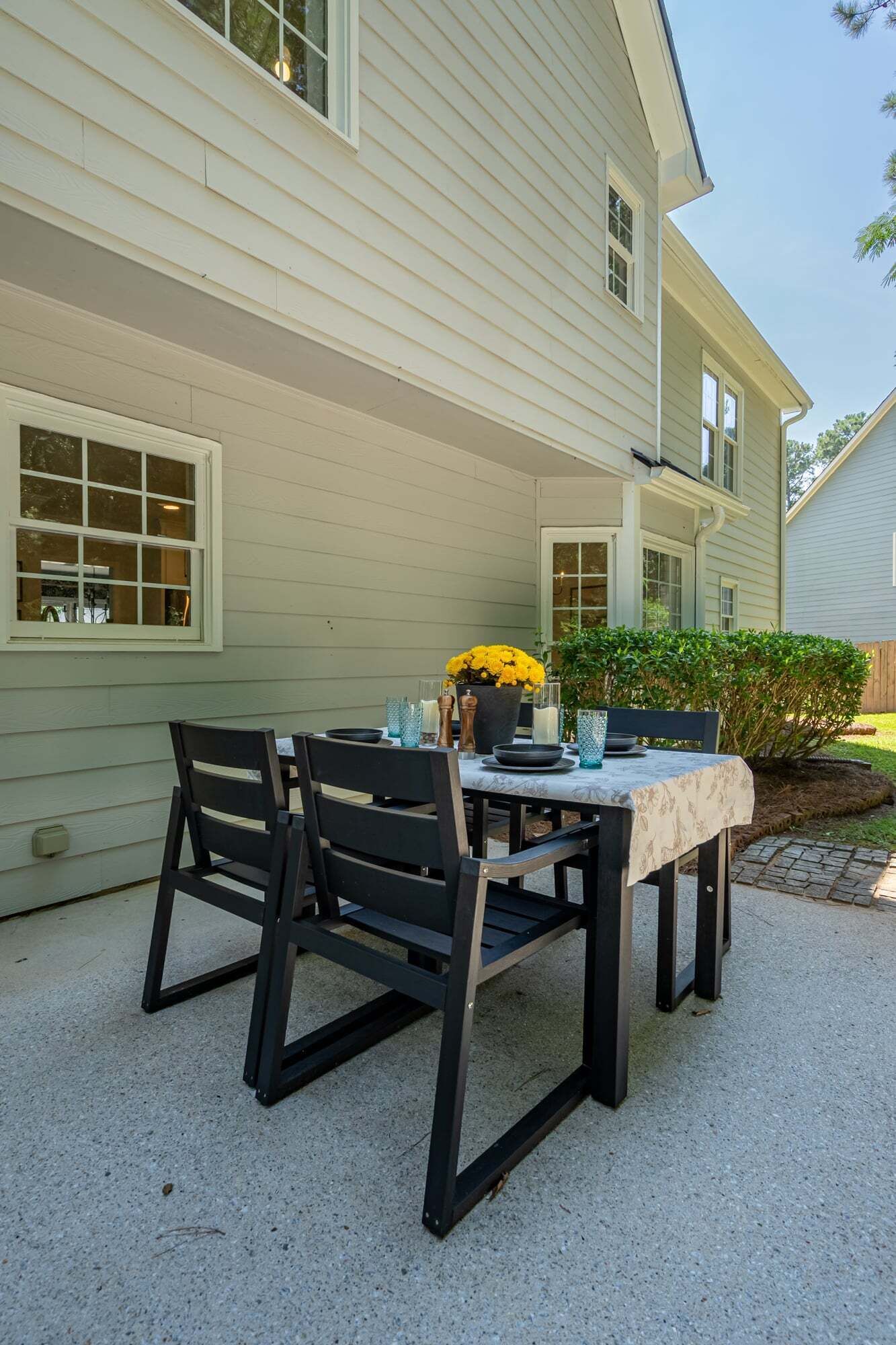An outdoor patio with a table set for dining, surrounded by a house with a light-colored exterior.