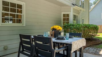 An outdoor patio with a table set for dining, surrounded by a house with a light-colored exterior.