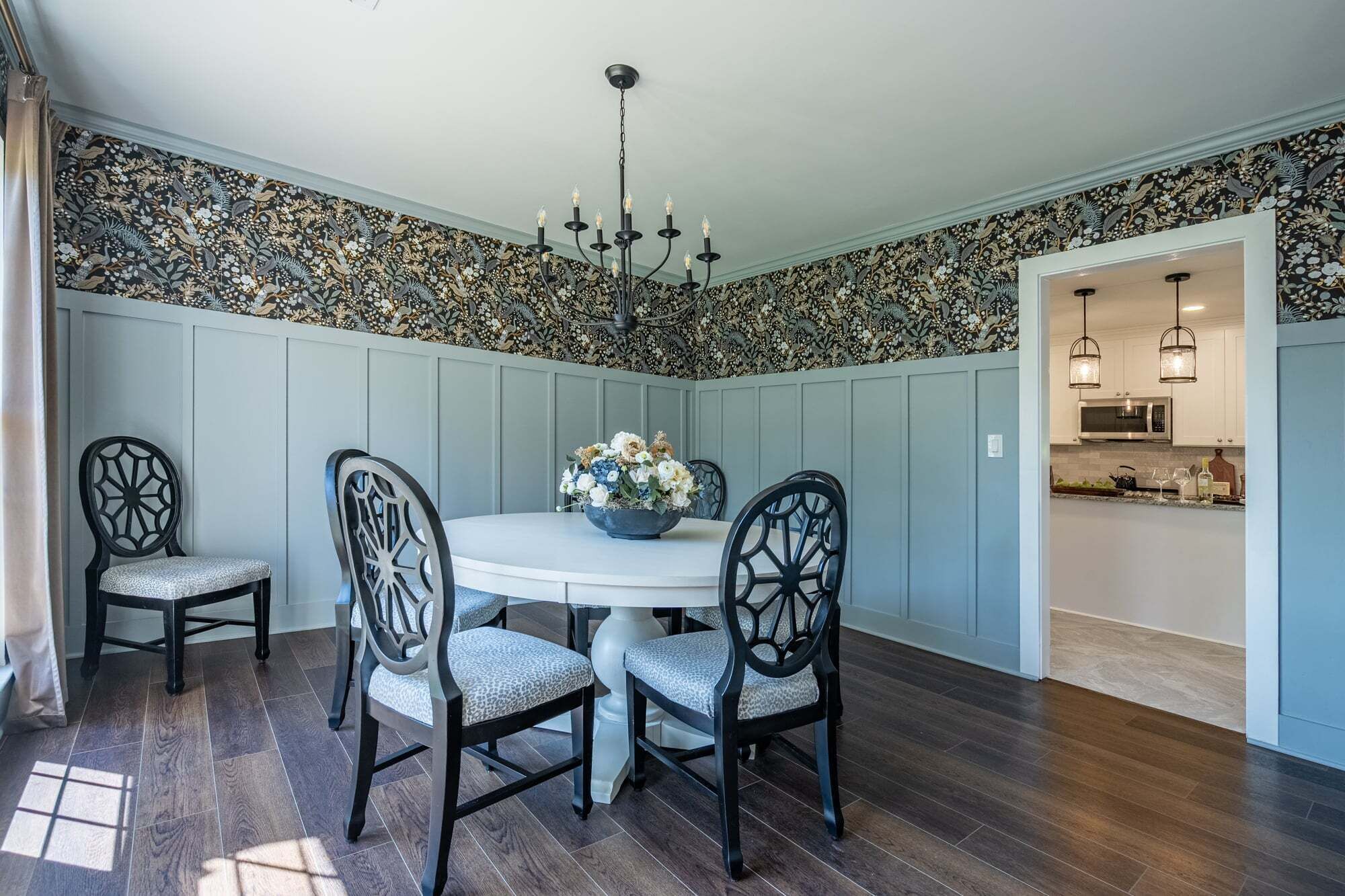 A dining area with a round table, four chairs, and a chandelier.