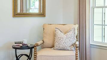 A room with a wooden chair, a small table, a mirror, and a window with curtains.