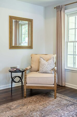 A room with a wooden chair, a small table, a mirror, and a window with curtains. - Spacious 4BR Retreat with Fire Pit near LakePoint (Acworth)