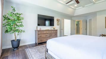 A bedroom with a large bed, a dresser, a television, and a ceiling fan.