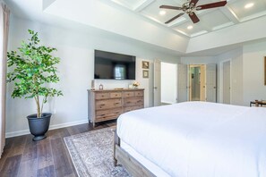 Un dormitorio con una cama grande, un aparador, un televisor y un ventilador de techo.