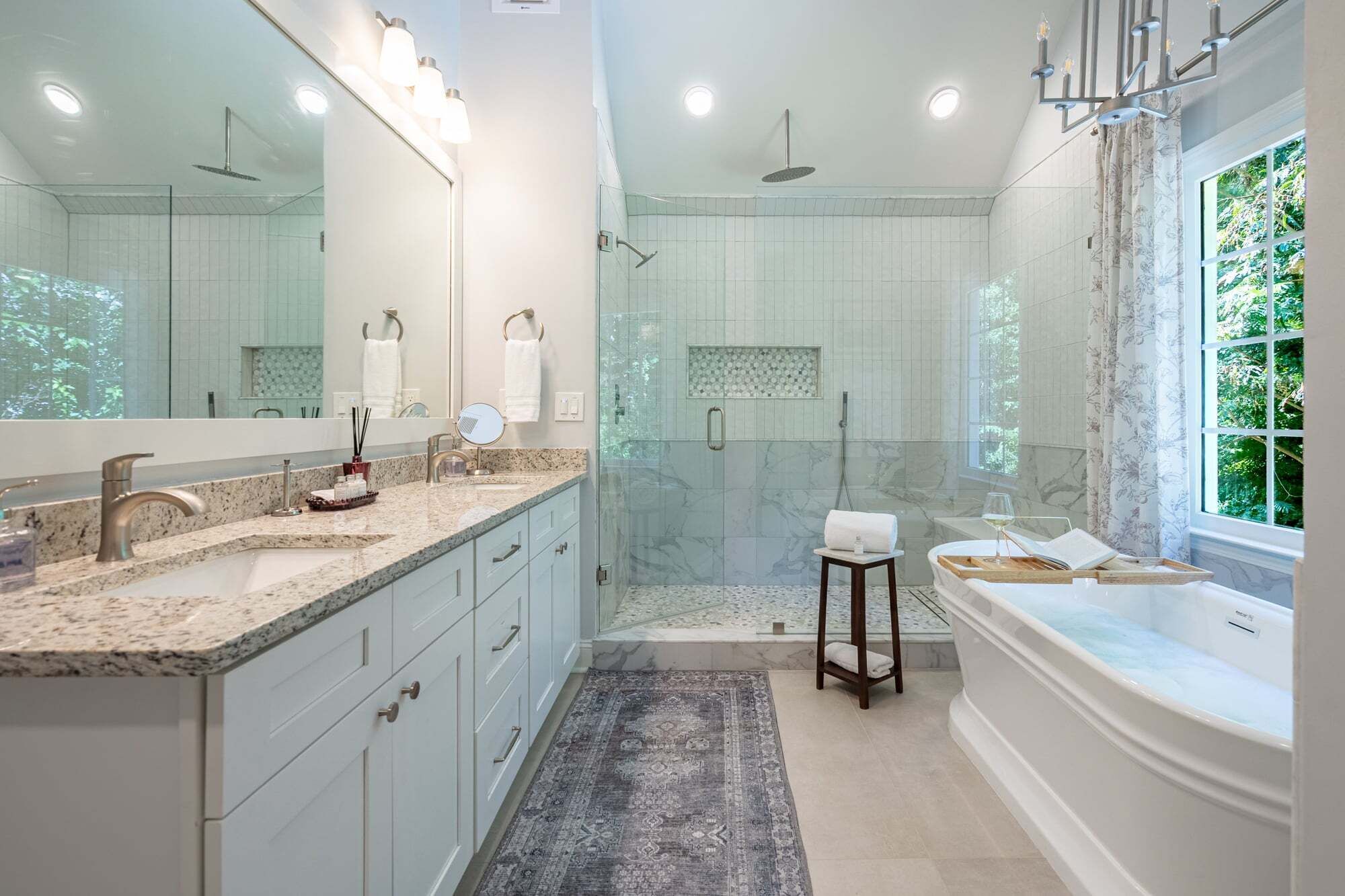 A modern bathroom with a large mirror, dual sinks, a walk-in shower, and a bathtub.