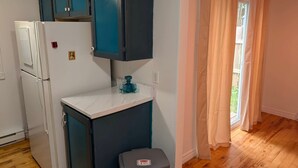 A compact kitchen with a white refrigerator, teal cabinets, a marble countertop, and a small stool.
