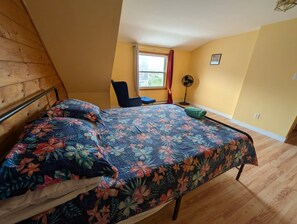 A bedroom with a bed, a chair, a window, and a fan.