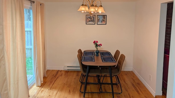 A dining area with a wooden table, chairs, a vase with flowers, and a chandelier.