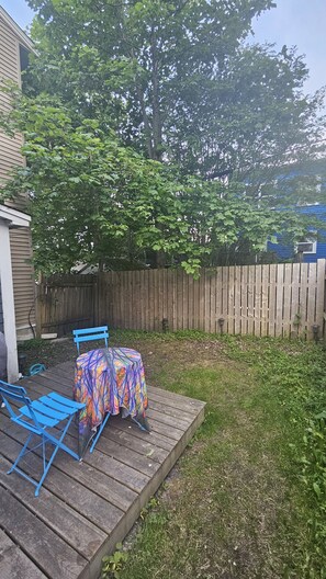 A backyard with a wooden deck, a table with a colorful tablecloth, and blue chairs.