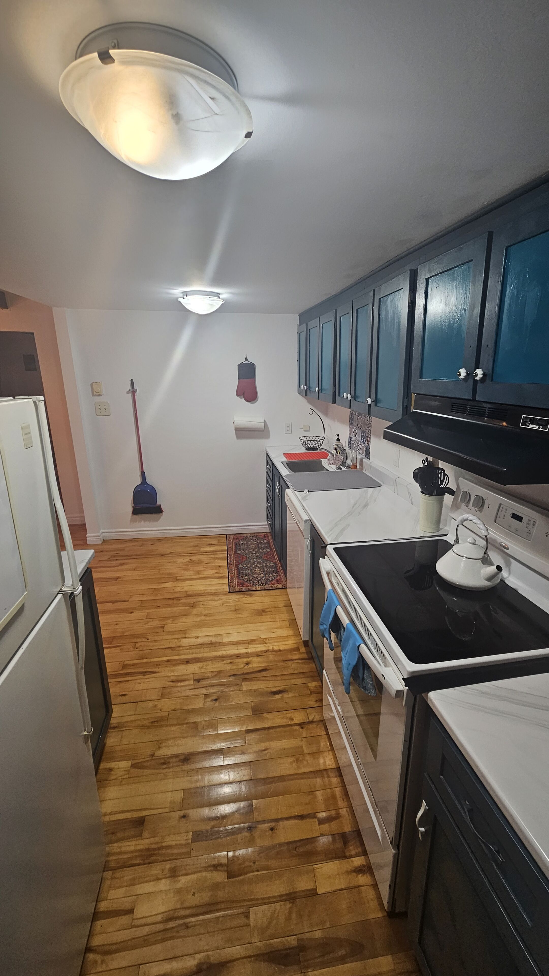 Uma cozinha com piso de madeira, fogão, armários e luminária no teto.
