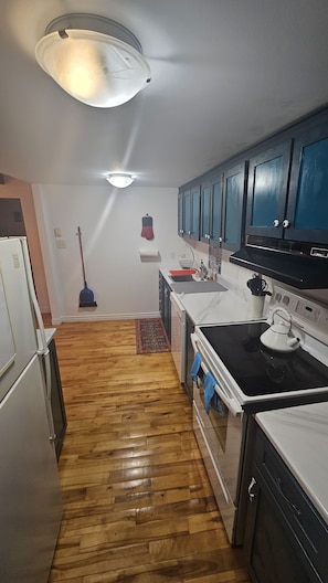 Una cocina con piso de madera, estufa, alacenas y una lámpara en el techo.