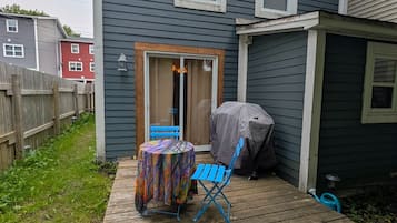 A wooden deck with a table and chairs, a covered grill, and a house with a blue exterior.