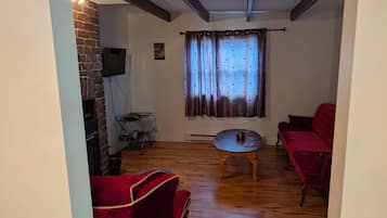 Ein Wohnzimmer mit einer Ziegelwand, einem flachbildfernseher, der darüber angebracht ist, einem roten Sofa, einem Holztisch und einem Fenster mit gemusterten Vorhängen.