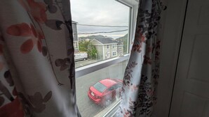 A window with a view of a red car on the street, a house, and a power line.