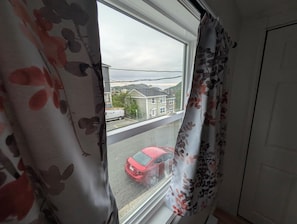 Una ventana con vista a un coche rojo en la calle, una casa y una línea de electricidad.