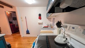 A kitchen with a stove, oven, and microwave. There is a broom and mop on the wall.