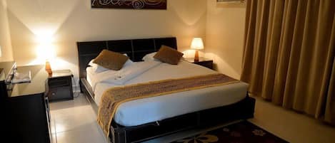 Una habitación de hotel con cama, mesitas de noche, un escritorio y una lámpara.