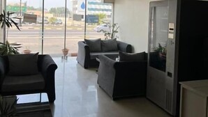 Zona de recepción con asientos, un refrigerador y vistas a la calle a través de amplios ventanales.