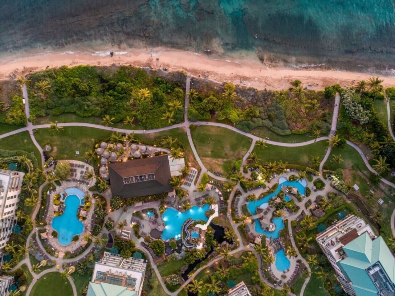 An aerial view of a resort with multiple swimming pools, a large building, and a beach.