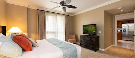 Habitación de hotel con cama, televisor en una cómoda, ventilador de techo y vista a la cocina.