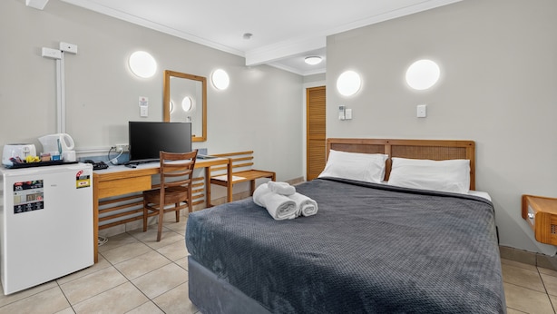 A hotel room with a bed, a desk with a computer, a chair, a small refrigerator, and a mirror. - Black Nugget Hotel (Moranbah)