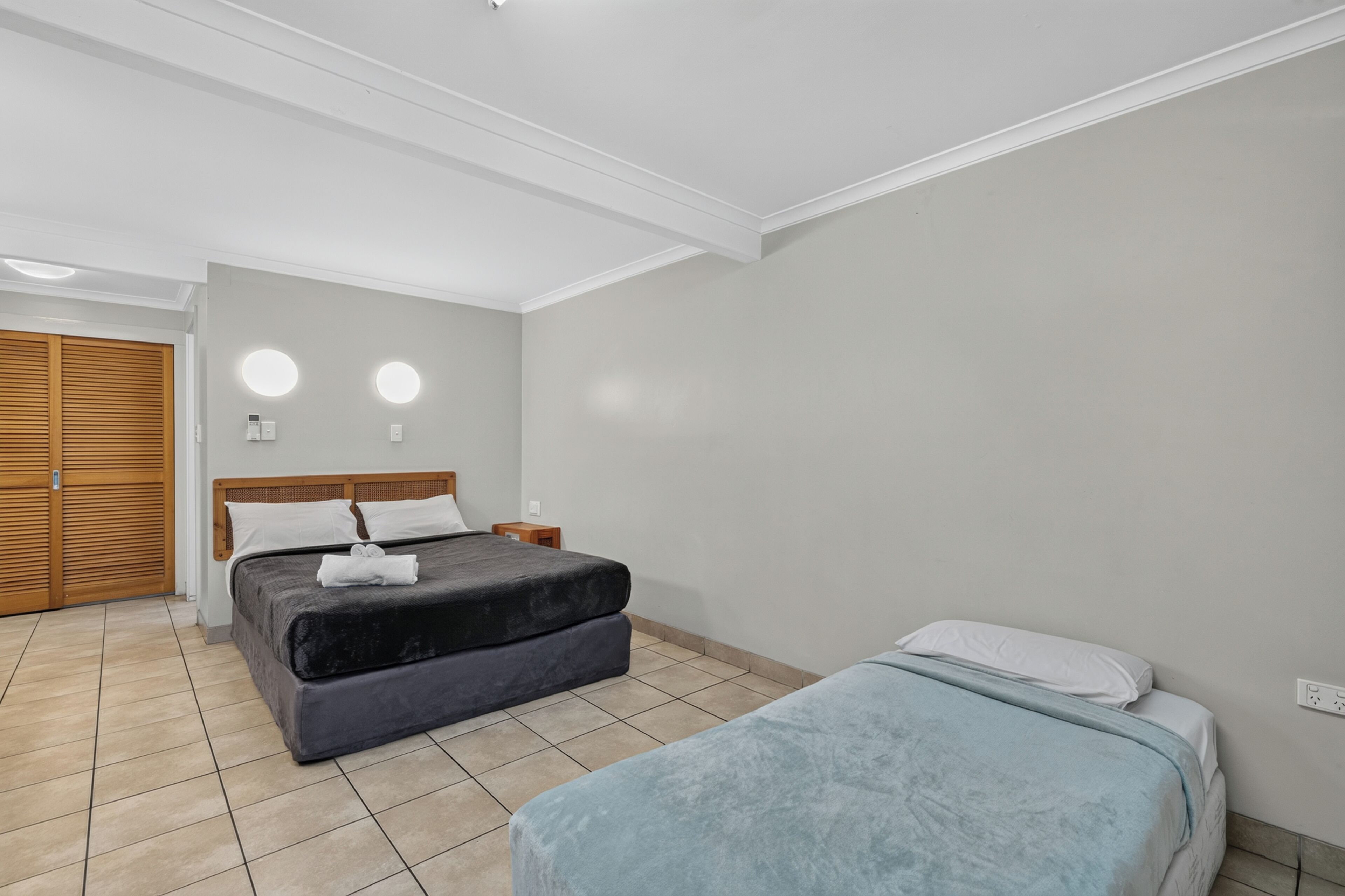 A hotel room with a bed, a bedside table, a wardrobe, and a small table with a lamp.