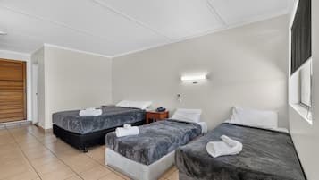 A hotel room with two beds, a bedside table, a wall-mounted light, and a window with blinds.