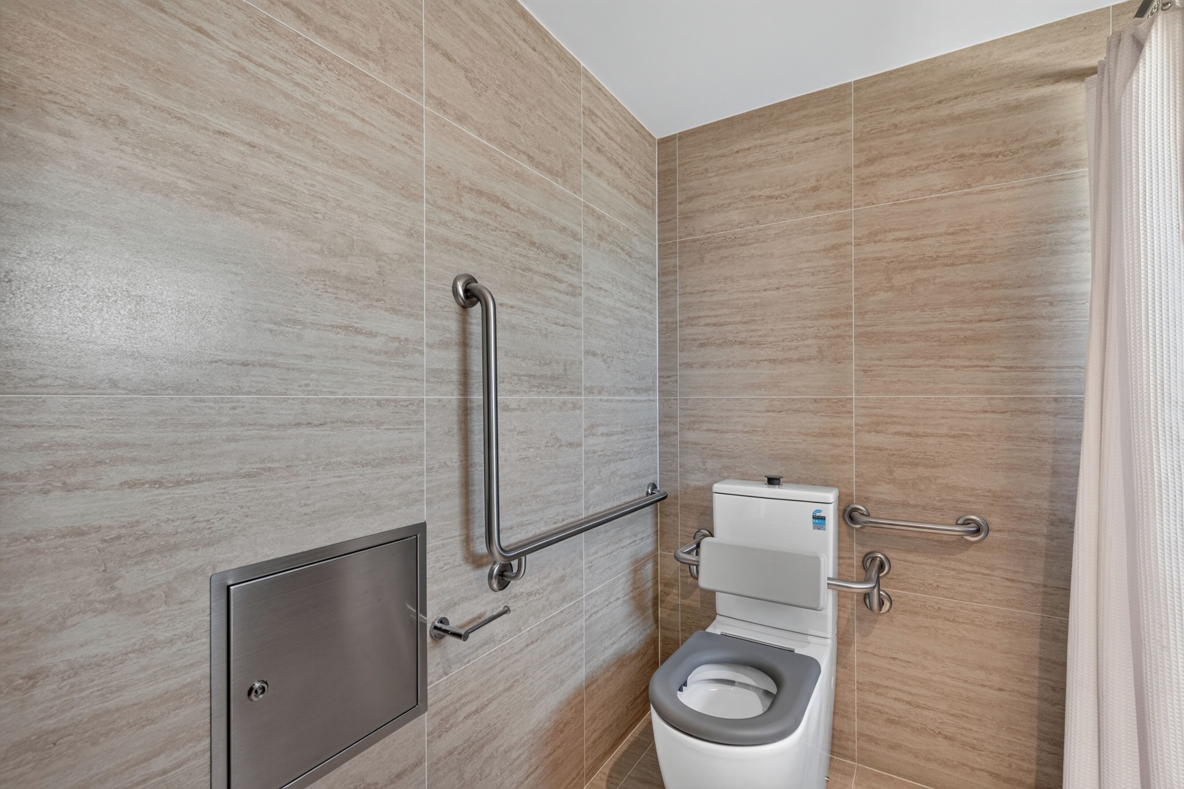 Un baño moderno con inodoro, barras de apoyo y cortina de ducha.