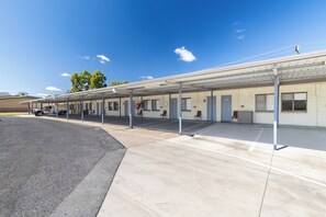 Un motel con estacionamiento techado, habitaciones numeradas y una camioneta de servicio.
