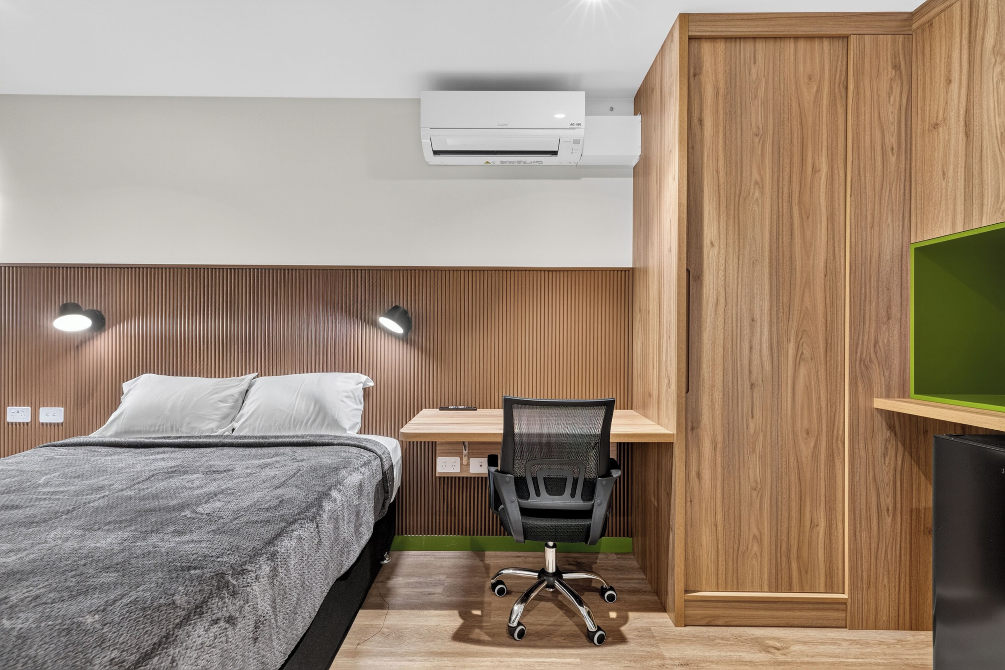 Un dormitorio moderno con cama, escritorio, silla y aire acondicionado.