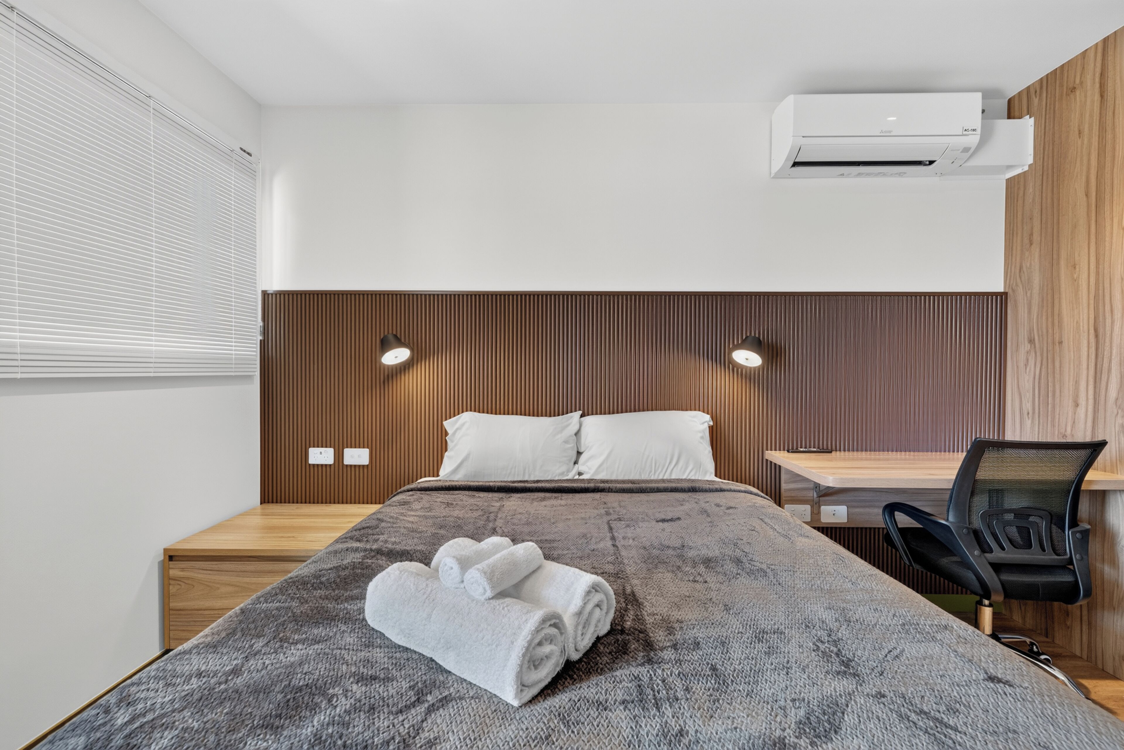 A modern hotel room with a bed, a desk, and an air conditioning unit.