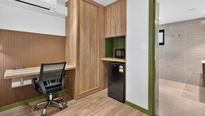 A modern office space with a wooden desk, a black office chair, a built-in air conditioner, and a compact refrigerator. - Black Nugget Hotel (Moranbah)