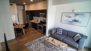 Un espacio habitable moderno con un sofá gris, una mesa de centro y una zona de cocina con estufa y microondas.