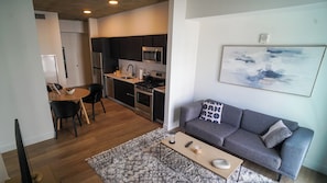 Ein modernes Wohnzimmer mit grauem Sofa, einem Couchtisch und einer Küchenzeile mit Herd und Mikrowelle.