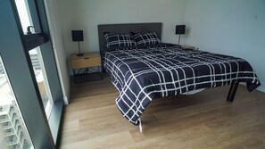 A bedroom with a bed, bedside tables, a lamp, and a view through a window. - 2-bedroom apartment in soothing Phoenix with AC and fitness room (Phoenix)