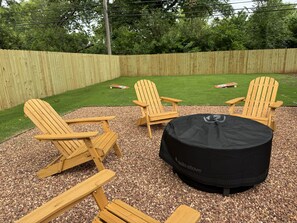 A backyard with a wooden deck, three Adirondack chairs, and a round black table with a cover.