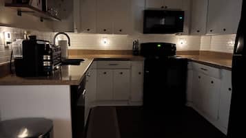 Una cocina con armarios blancos, microondas, cafetera y cubo de basura.